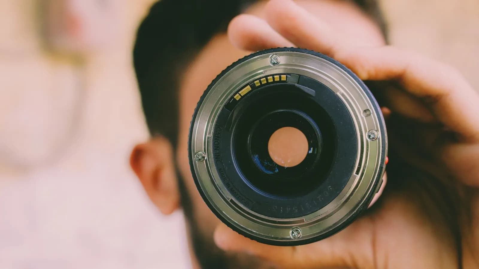 Nahaufnahme der Frontlinse eines Canon-Objektivs, vor das Gesicht des Fotografen gehalten.