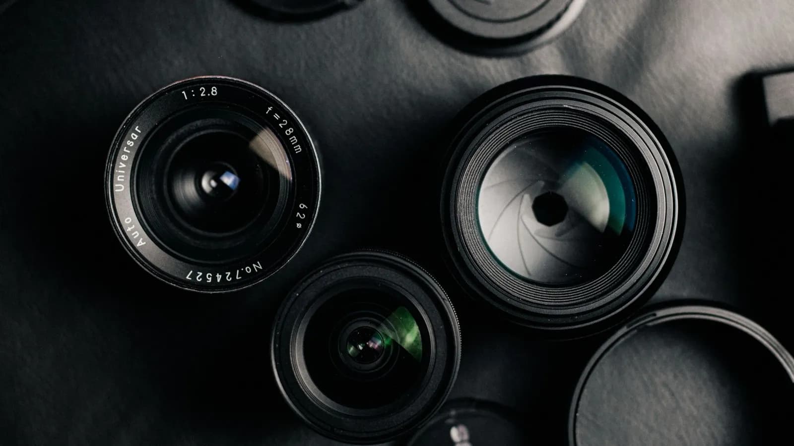 Mehrere Kameraobjektive flach auf dunklem Untergrund, darunter ein Vintage-28-mm-f/2,8-Objektiv.